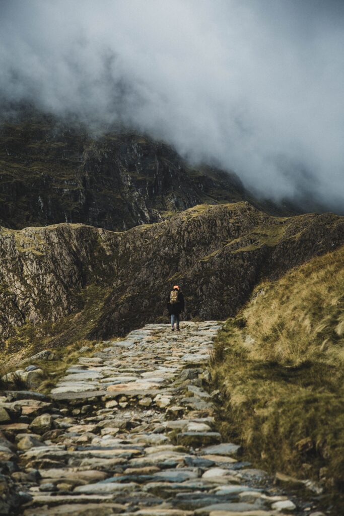 someone walking up a path to a cloudy crag