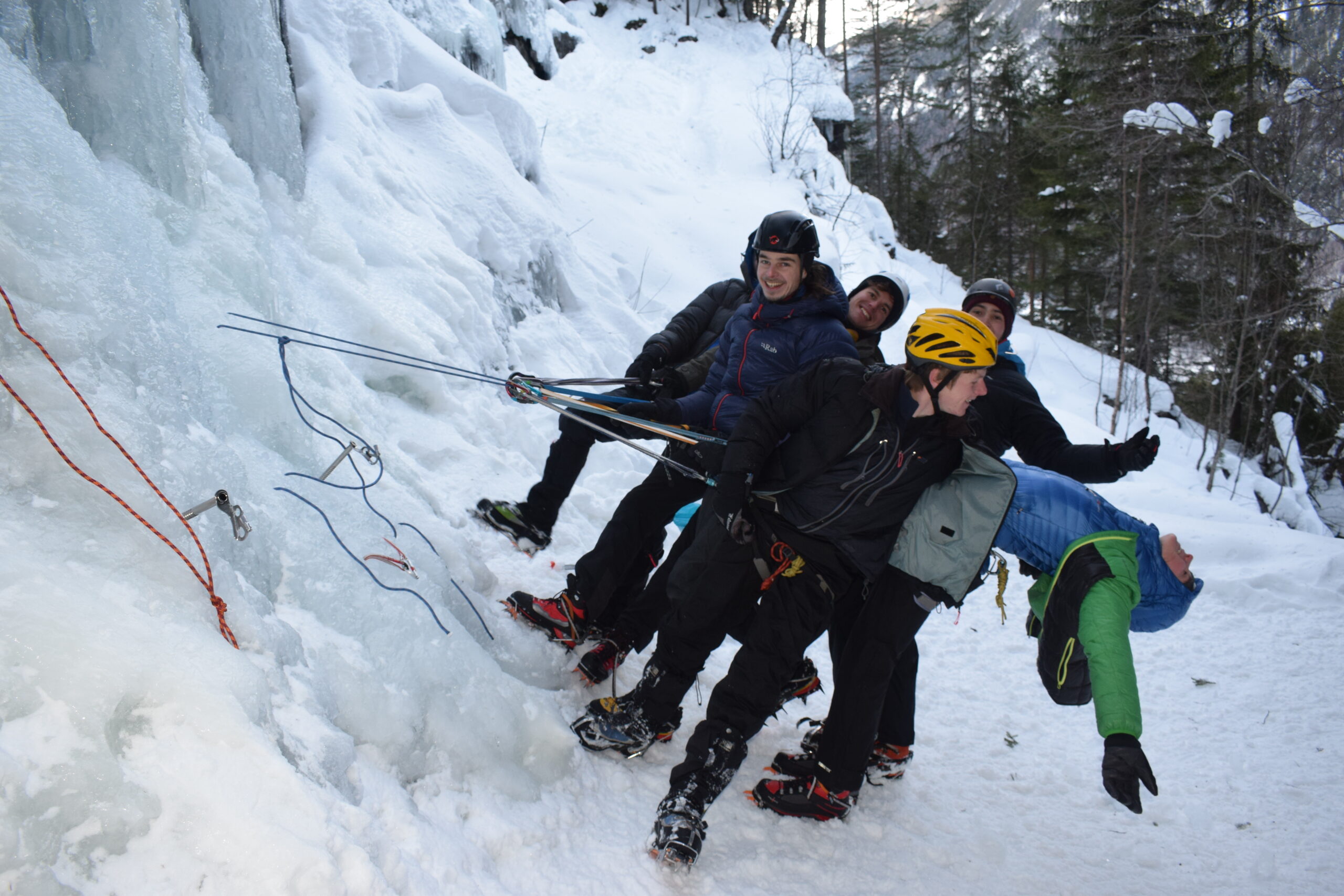A group of people using winter climbing gear at an icy cliff